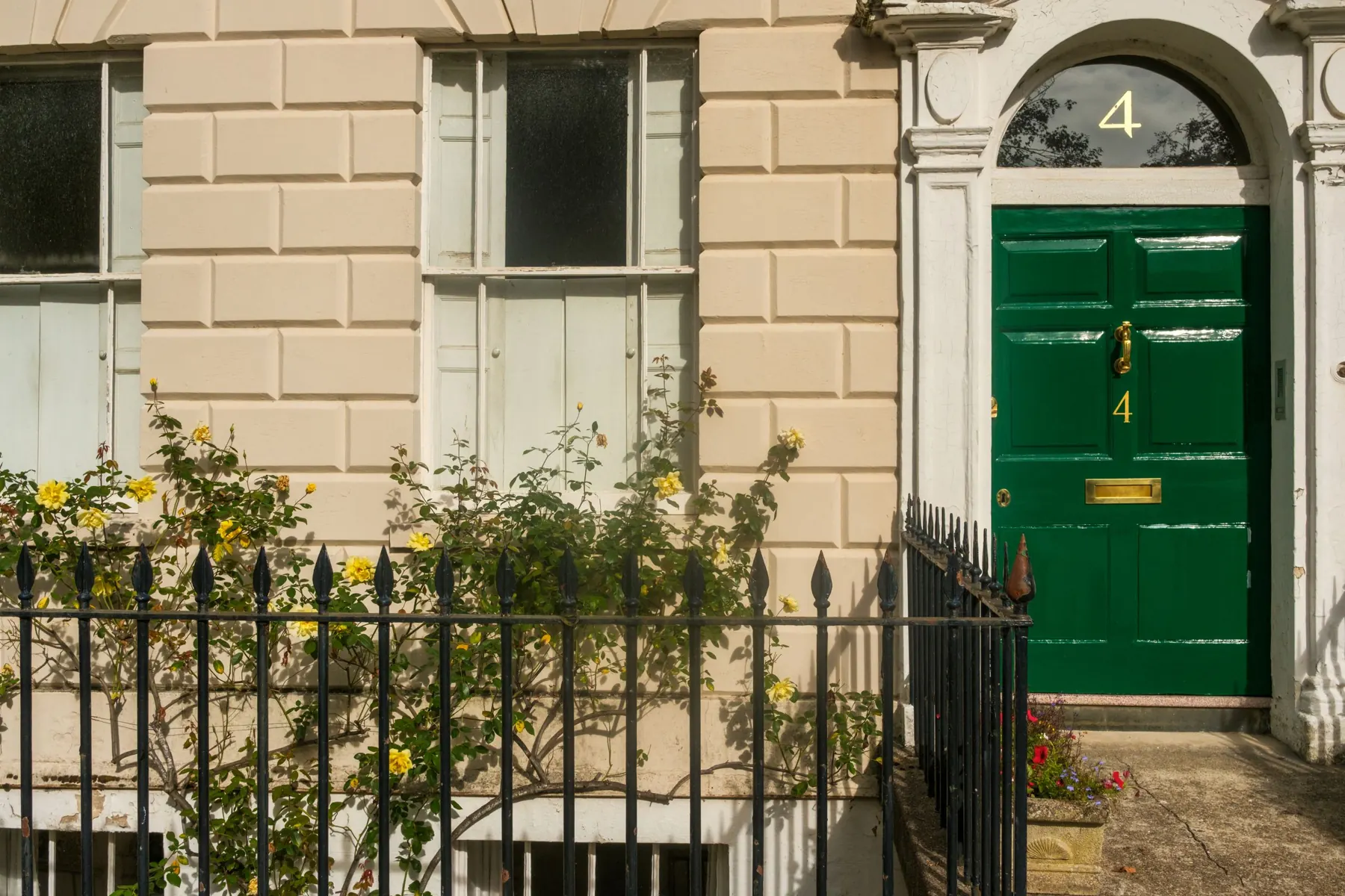 Green Georgian front door with a fanlight in a stone wall